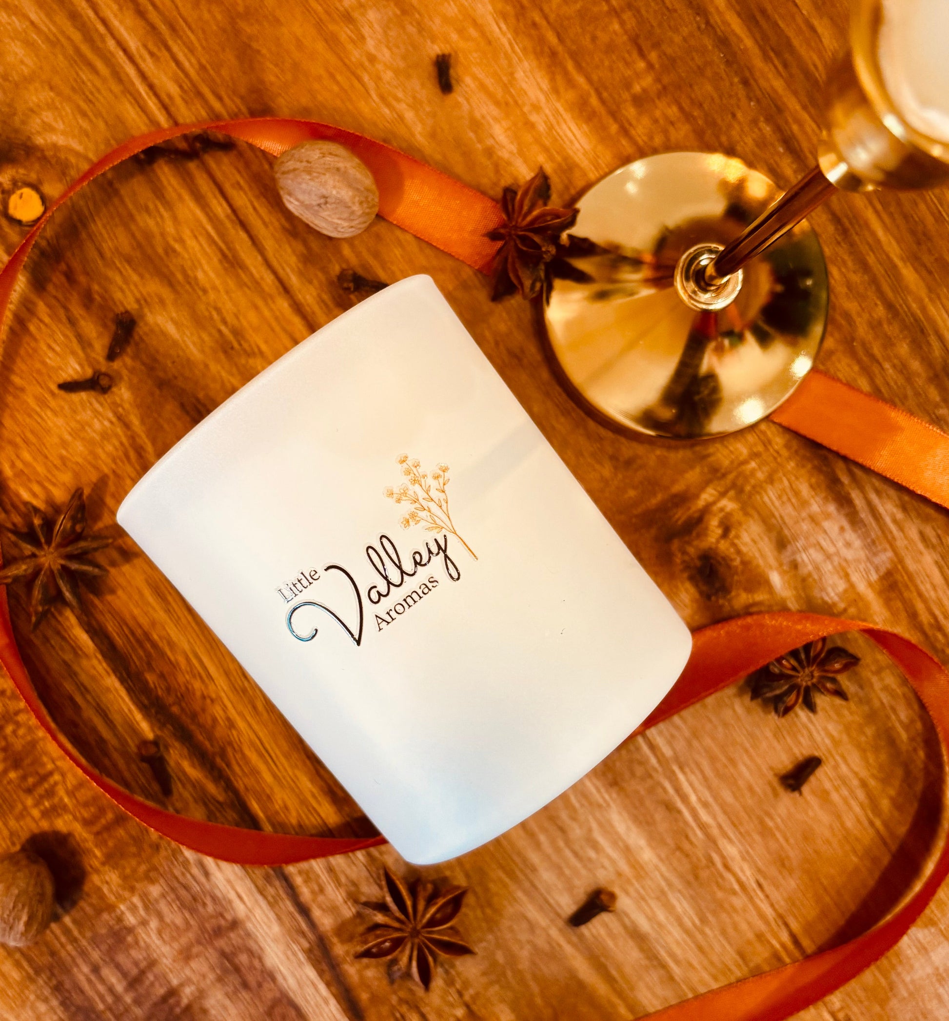 White candle with 'Little Valley Aromas' branding on a wooden surface with star anise and a gold candle holder.